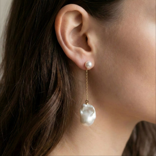 Model wearing mismatched baroque pearl earrings to show the length difference. One side hangs low on a chain, the other sits closer to the earlobe.