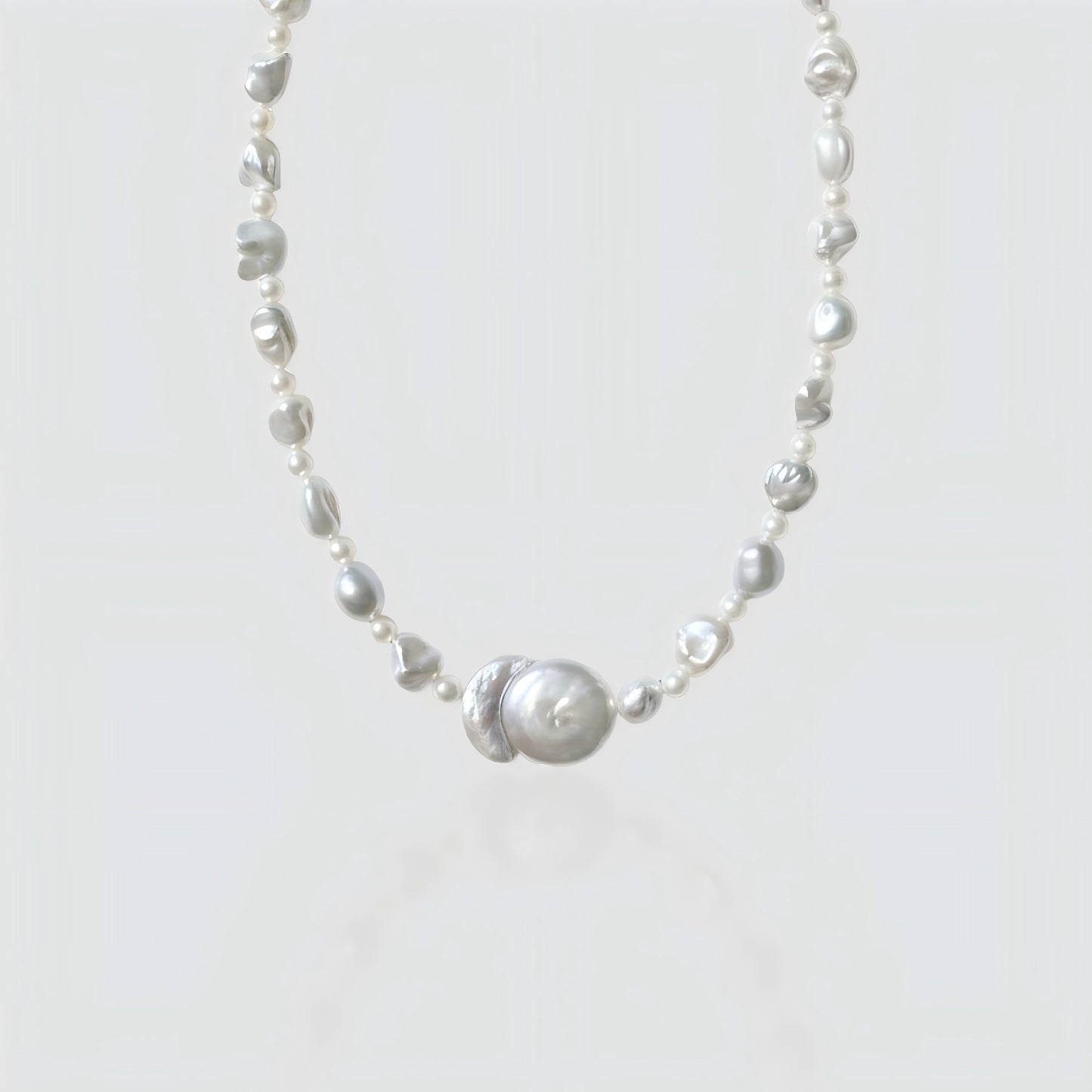 Studio shot of a freshwater baroque pearl necklace featuring a unique "Sun and Moon" center pendant, isolated on a white background.
