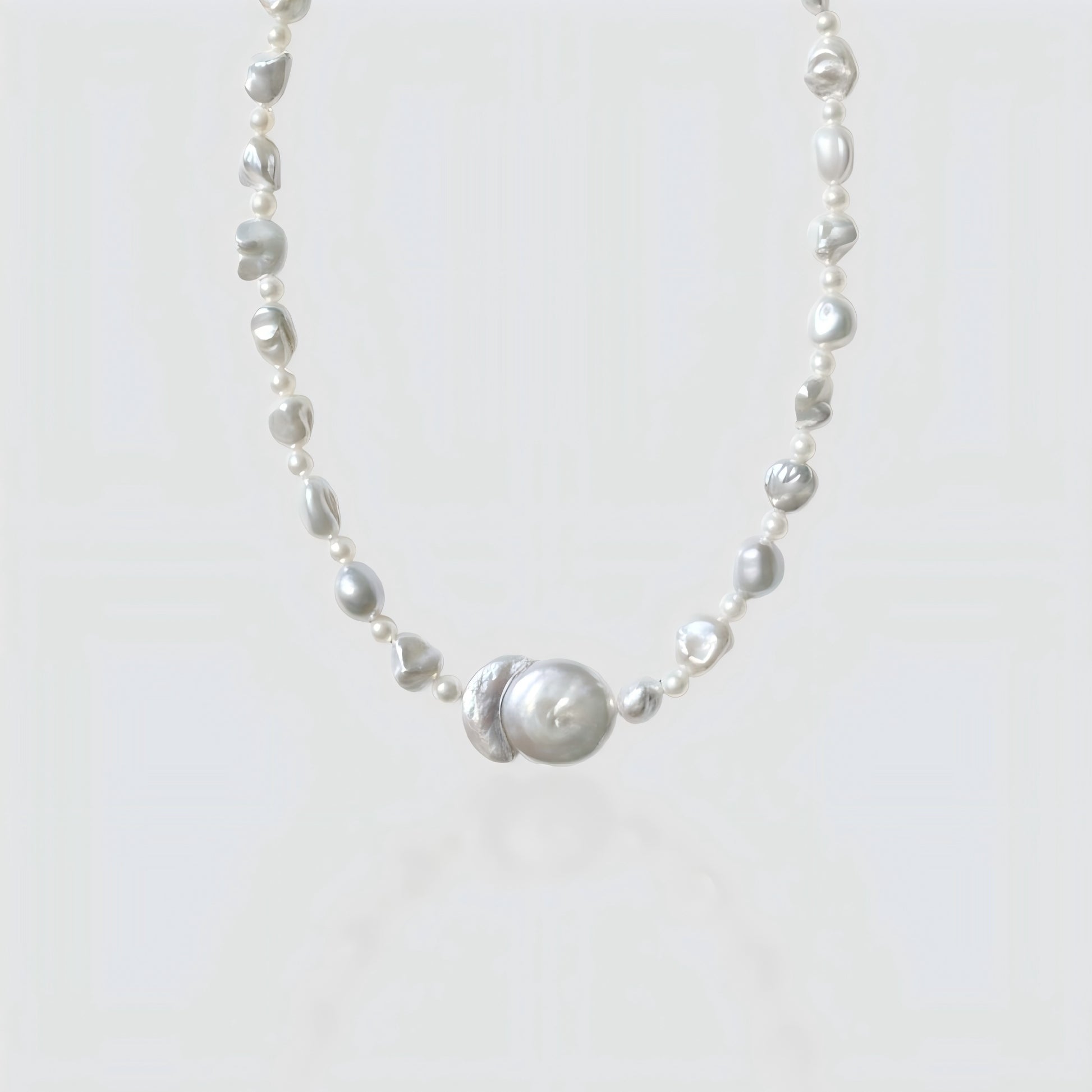 Studio shot of a freshwater baroque pearl necklace featuring a unique "Sun and Moon" center pendant, isolated on a white background.