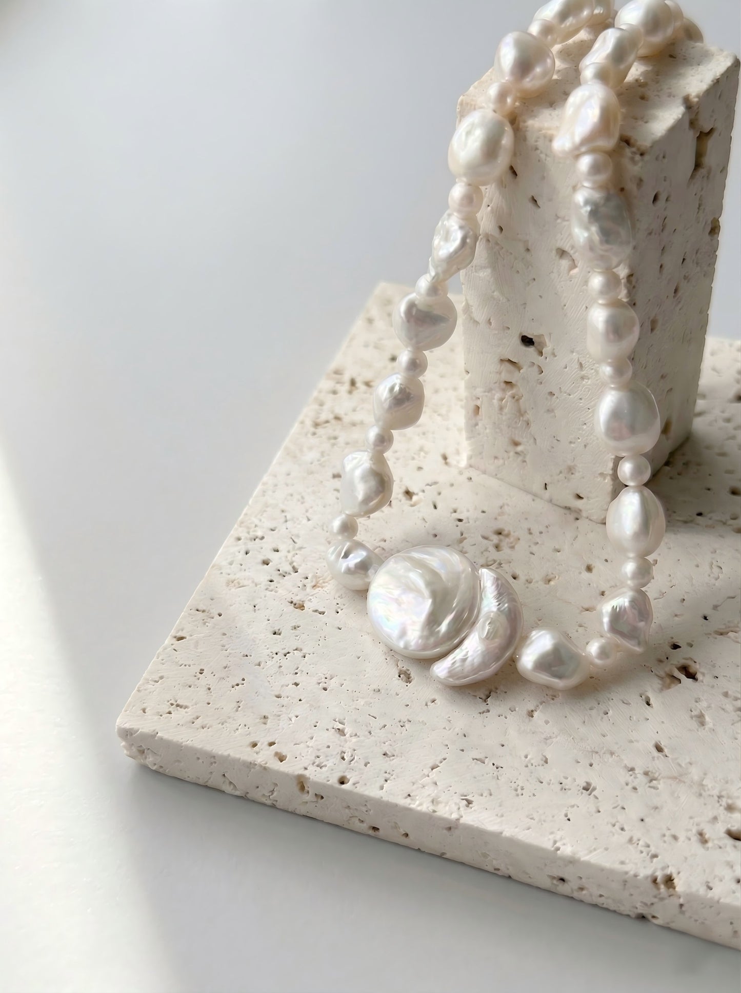 Close up details of natural freshwater baroque pearl and round pearl pendant on textured stone display, artisan handcrafted necklace.