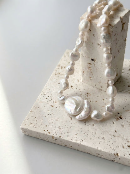 Close up details of natural freshwater baroque pearl and round pearl pendant on textured stone display, artisan handcrafted necklace.