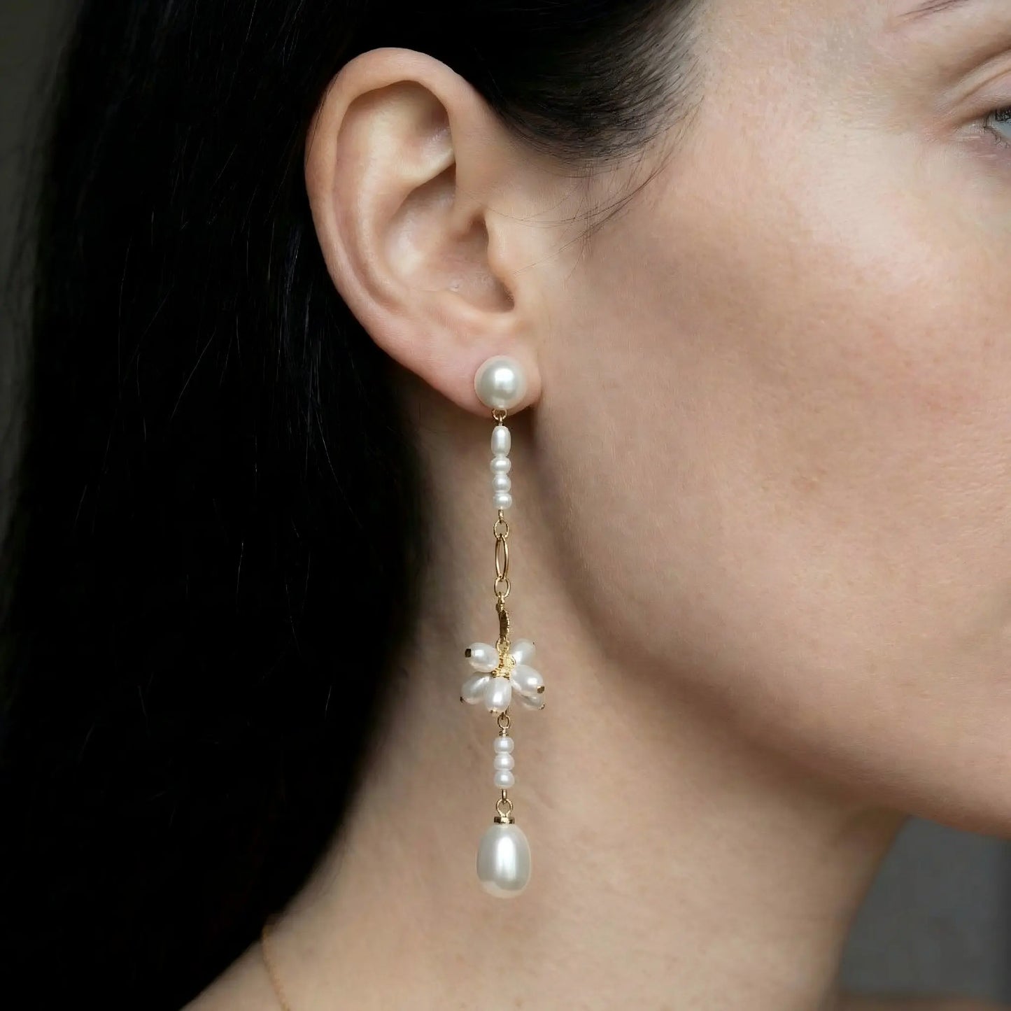 A model with styled hair wearing the Pearltide floral pearl drop earrings. The image shows the earrings dangling elegantly against the side of her neck, illustrating their long length and how the pearl luster catches the light. Perfect as bridal earrings or for formal events.