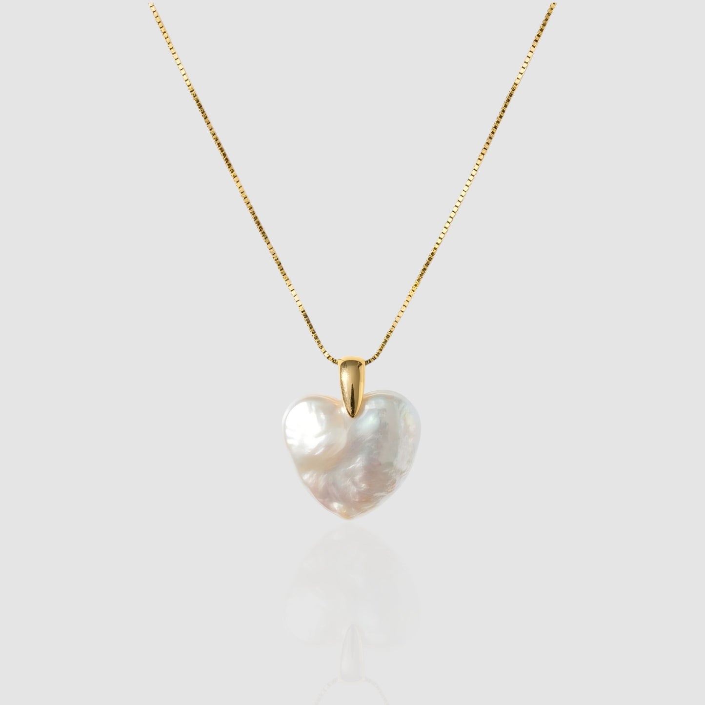 A lustrous, organic heart-shaped baroque pearl pendant hanging on a gold box chain against a light grey/white background.