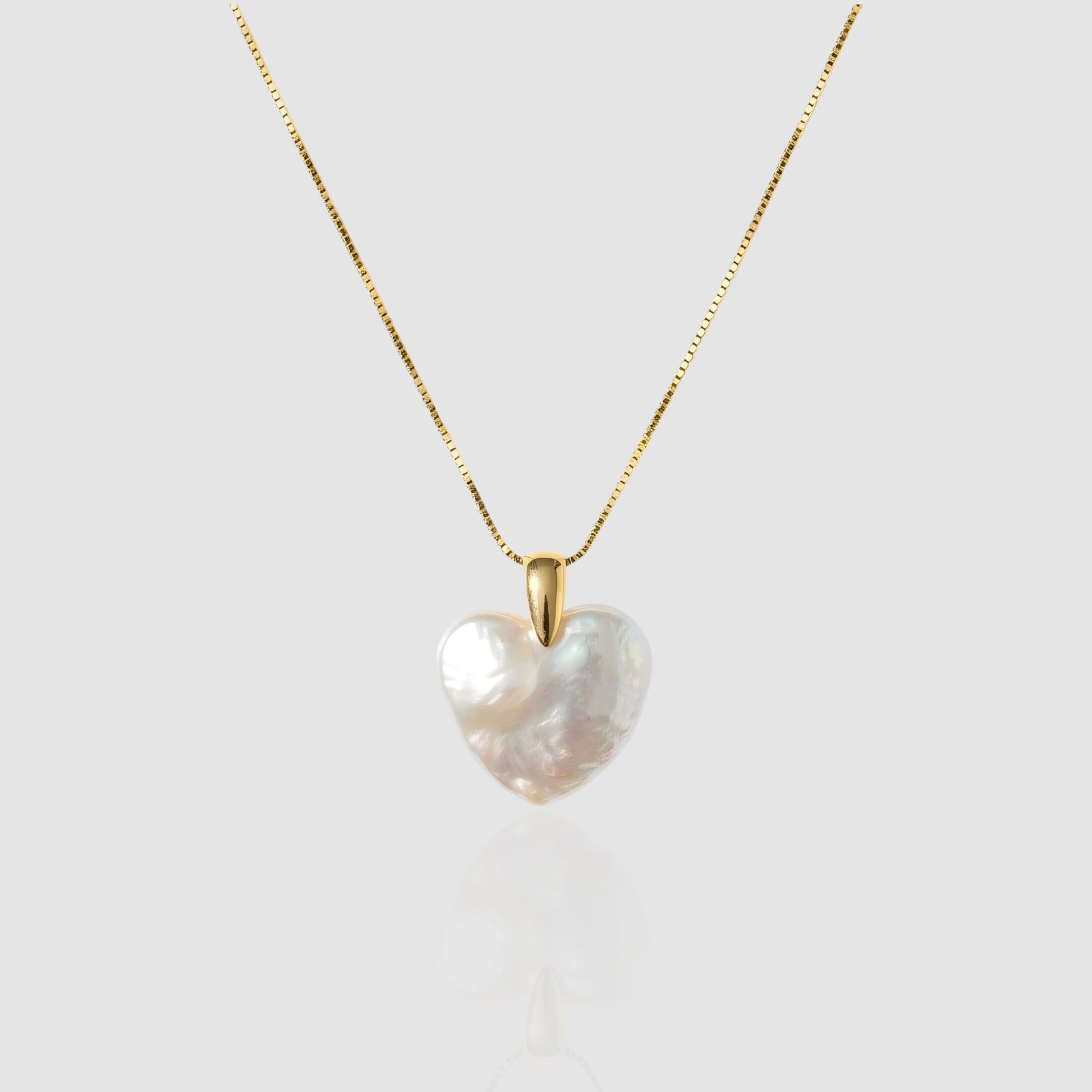 A lustrous, organic heart-shaped baroque pearl pendant hanging on a gold box chain against a light grey/white background.
