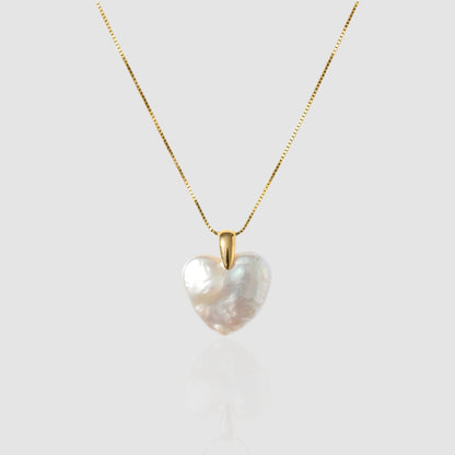 A lustrous, organic heart-shaped baroque pearl pendant hanging on a gold box chain against a light grey/white background.