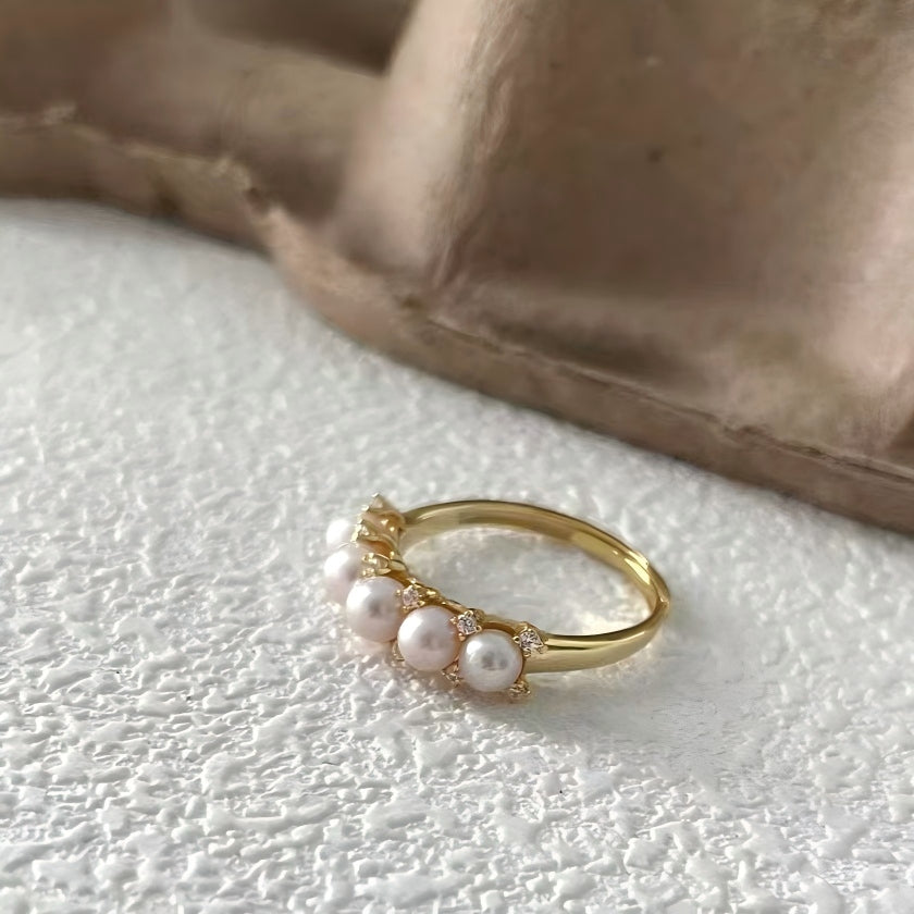 Close-up macro shot of pink freshwater pearls and pavé setting on a gold ring, highlighting the high-quality craftsmanship and texture.