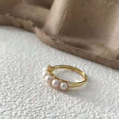 Close-up macro shot of pink freshwater pearls and pavé setting on a gold ring, highlighting the high-quality craftsmanship and texture.