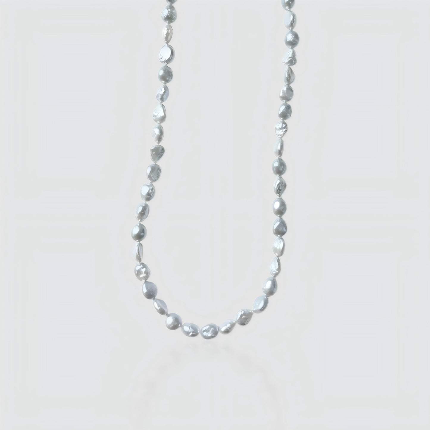 Studio shot of a silver-grey baroque pearl necklace with organic nugget shapes on a textured stone background.