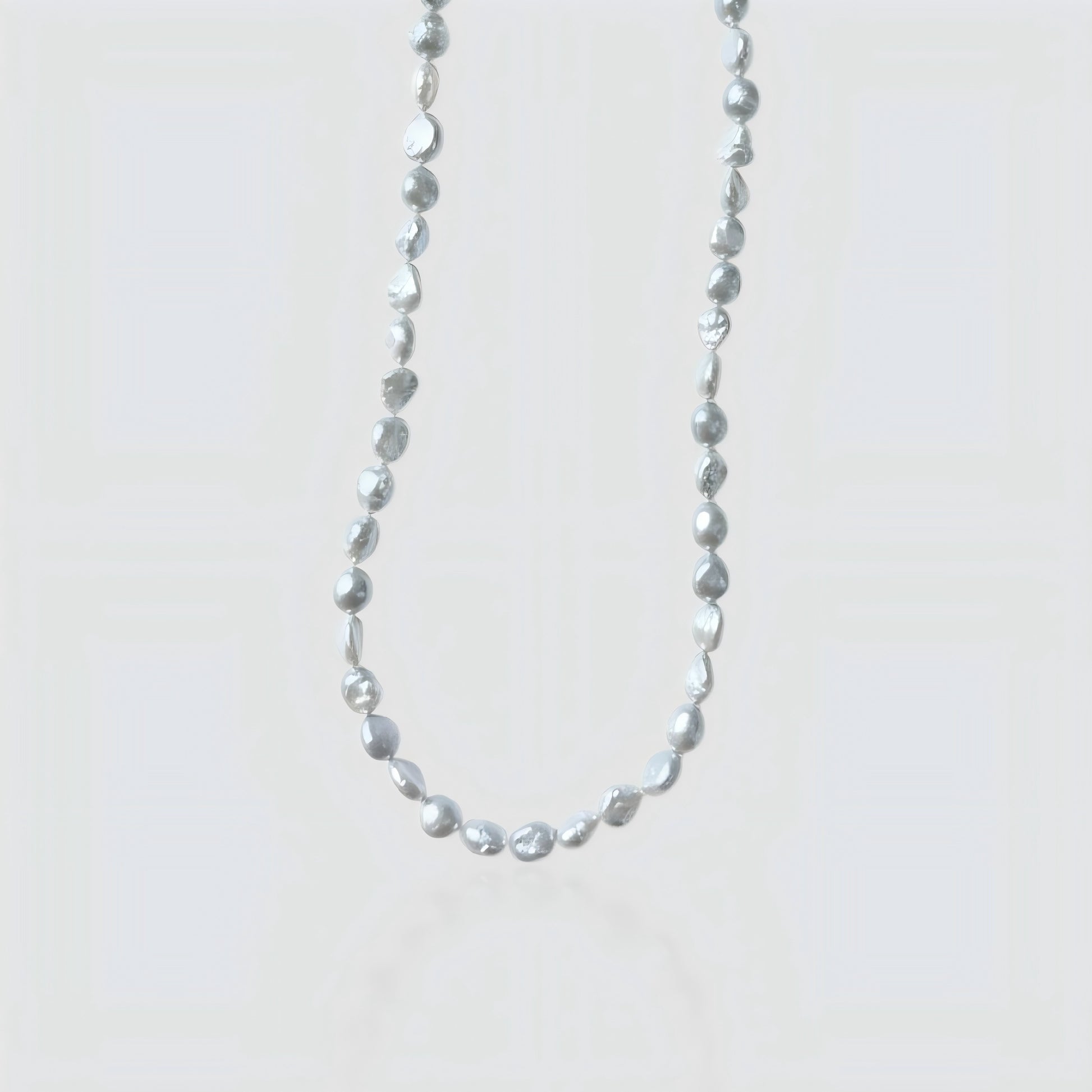 Studio shot of a silver-grey baroque pearl necklace with organic nugget shapes on a textured stone background.