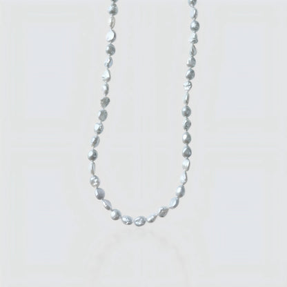 Studio shot of a silver-grey baroque pearl necklace with organic nugget shapes on a textured stone background.