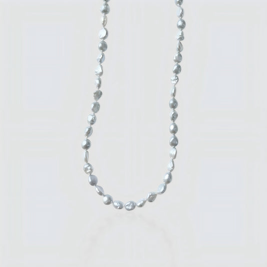 Studio shot of a silver-grey baroque pearl necklace with organic nugget shapes on a textured stone background.