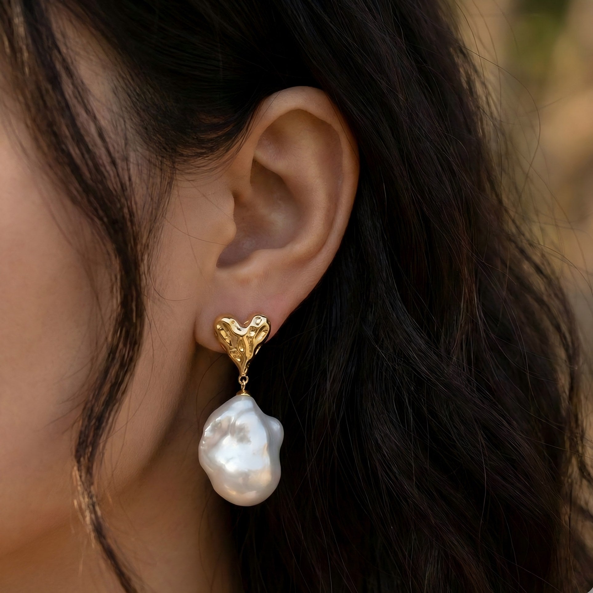 Elegantly framing the jawline. See how the baroque pearl drop adds a soft, moving glow that complements the warm gold heart.