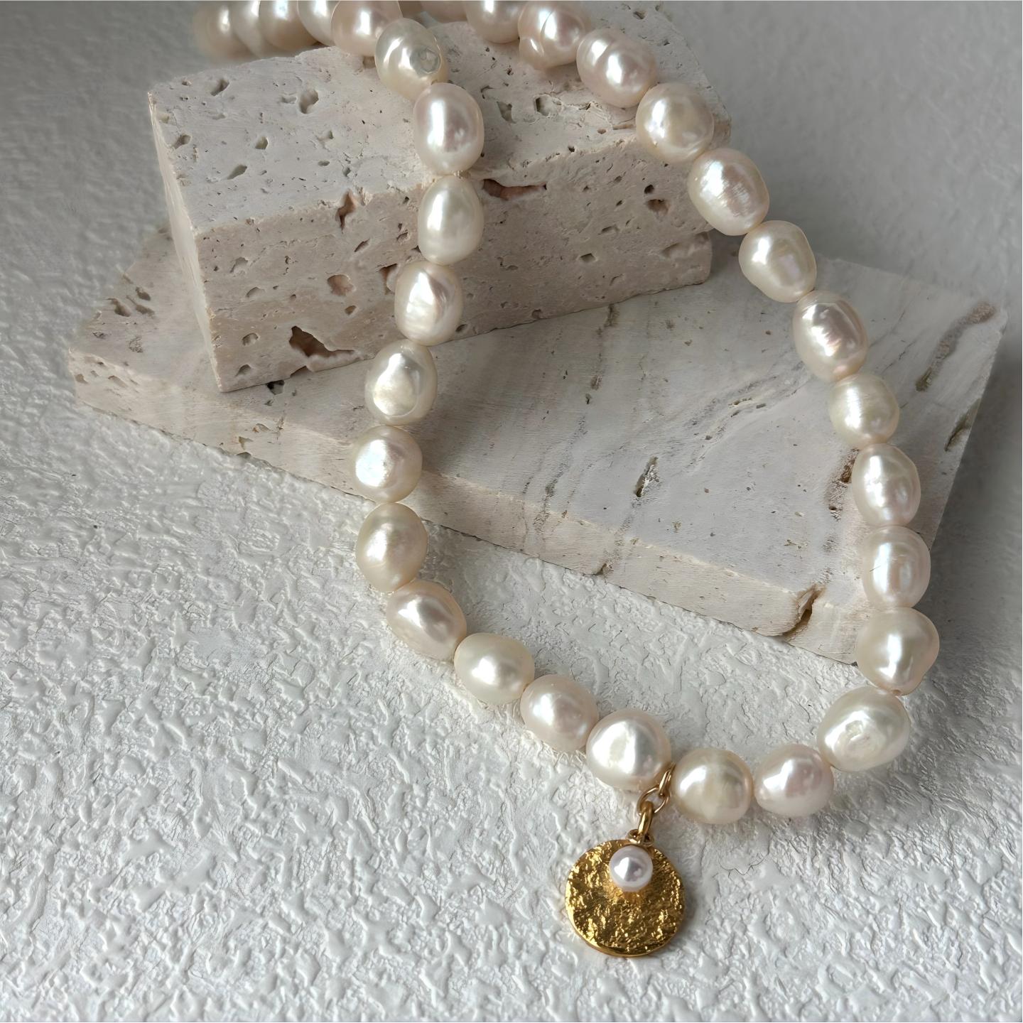 Macro detail shot of the hammered gold disc pendant attached to a pearl strand. Close-up showing the tiny seed pearl set in the textured gold charm.