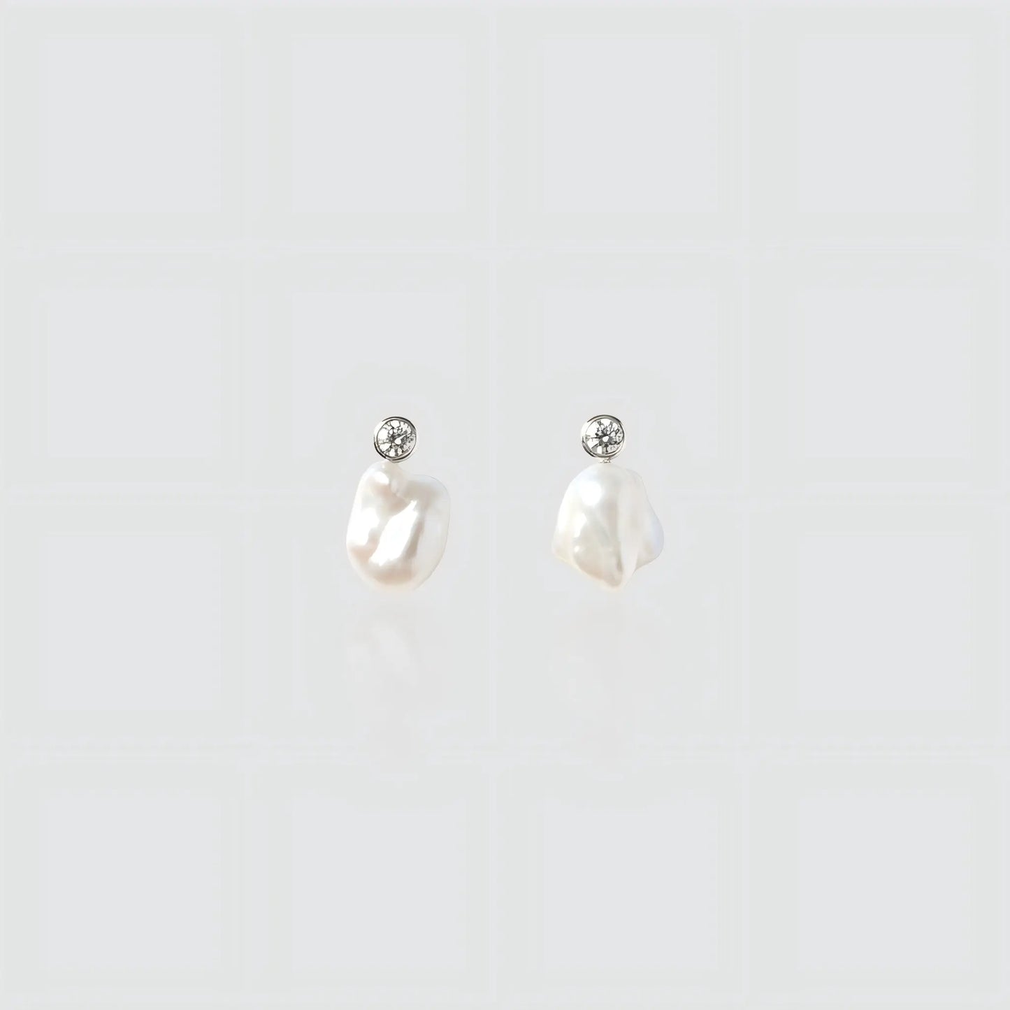A pair of silver drop earrings featuring small irregular freshwater pearls hanging from round bezel-set cubic zirconia studs.