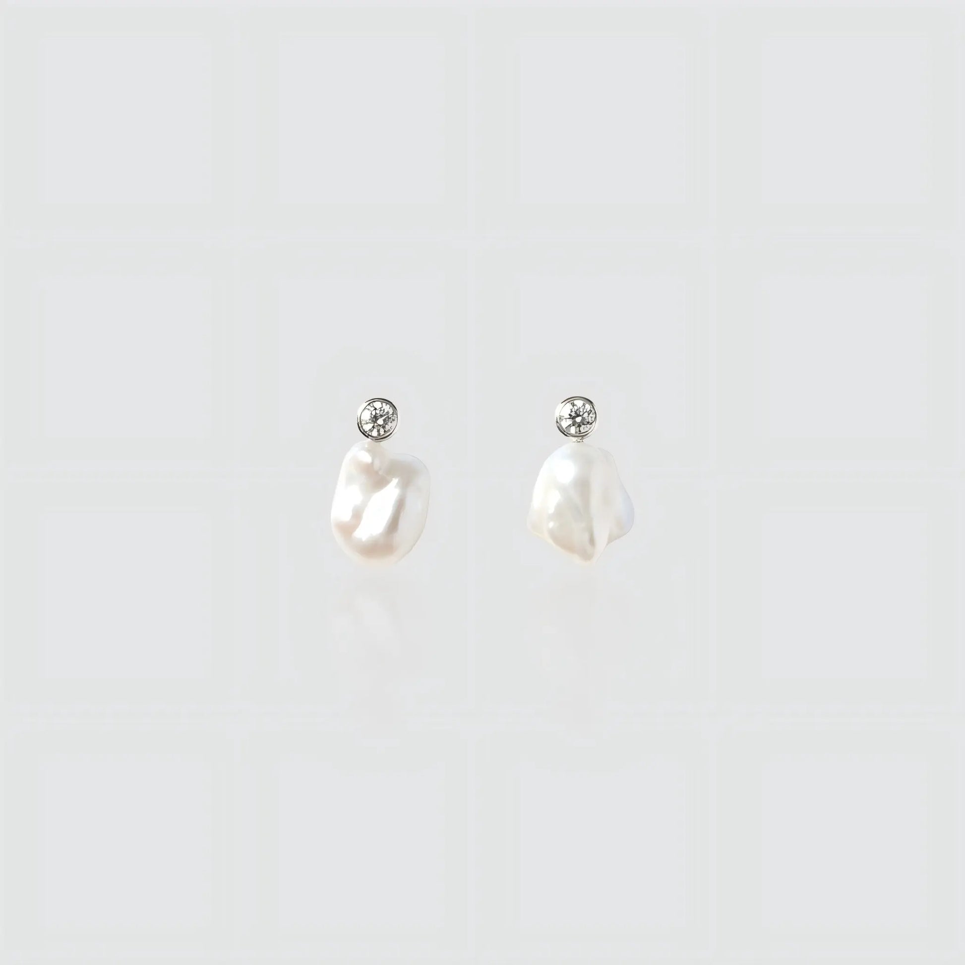 A pair of silver drop earrings featuring small irregular freshwater pearls hanging from round bezel-set cubic zirconia studs.