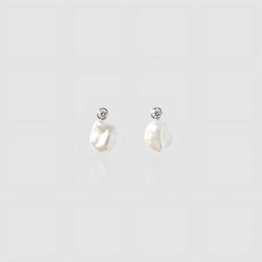 A pair of silver drop earrings featuring small irregular freshwater pearls hanging from round bezel-set cubic zirconia studs.