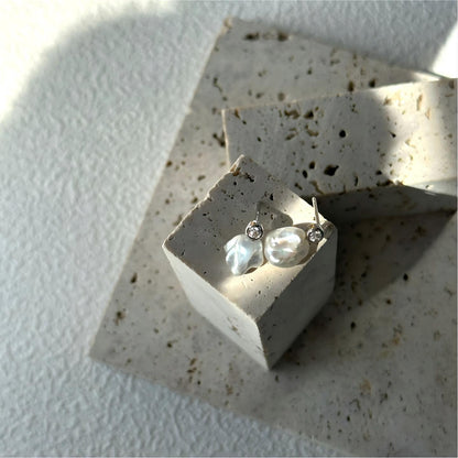 Close-up detail of the connection between the bezel-set sparkling stud and the organic white baroque pearl.