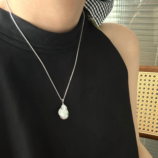 Woman wearing a minimalist Baroque pearl necklace with a white shirt. Elegant daily jewelry styling for women. Close-up of pearl pendant on neck.