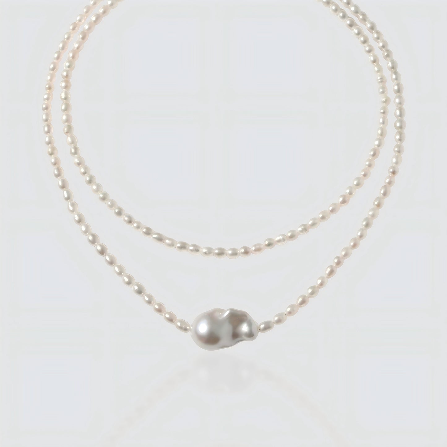 White background shot of a baroque pearl necklace with a unique asymmetrical "Sun and Moon" pendant.