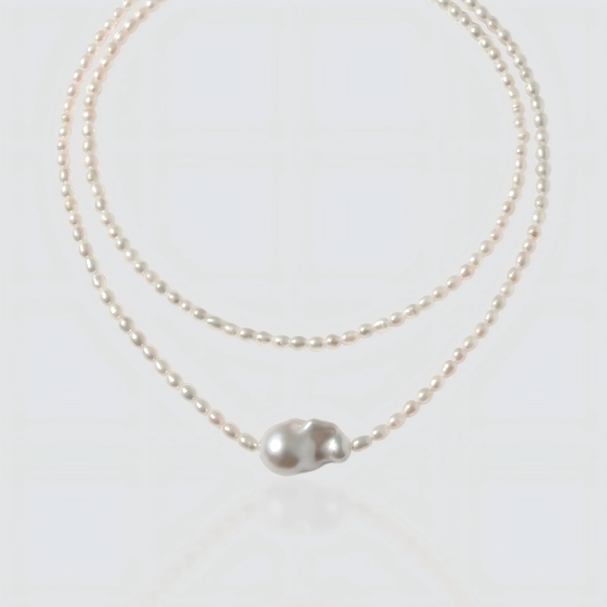 White background shot of a baroque pearl necklace with a unique asymmetrical "Sun and Moon" pendant.