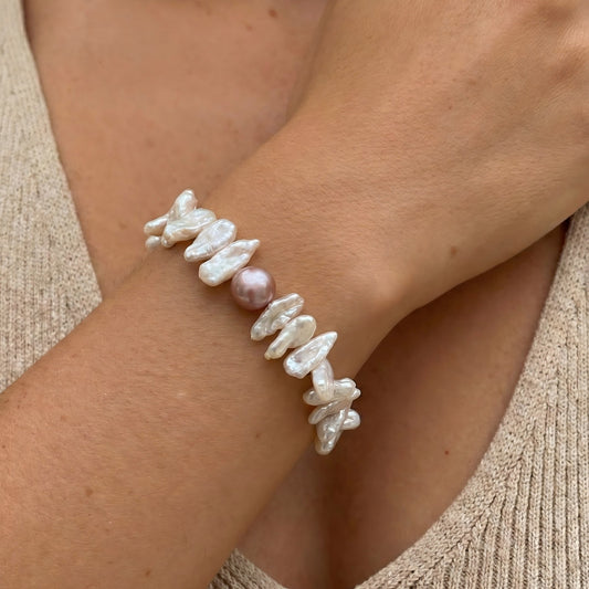 Close-up of a woman's wrist wearing an organic keshi pearl bracelet that looks like a flower wreath, styled with a soft linen outfit.
