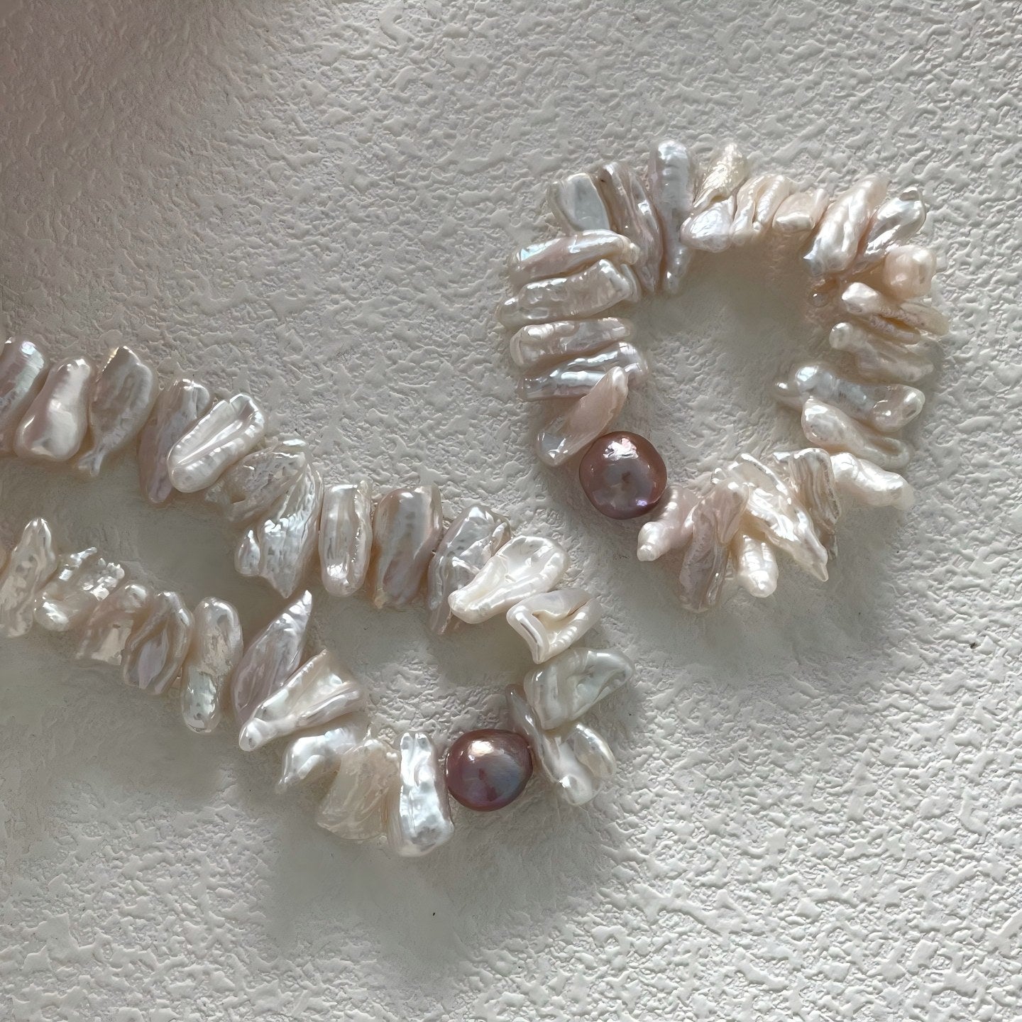 Macro detail showing the high luster and irregular petal shape of white keshi pearls next to a smooth, round metallic purple freshwater pearl.