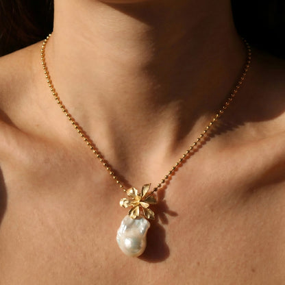 A woman wearing a romantic gold flower and baroque pearl necklace, styled with a soft, feminine outfit.