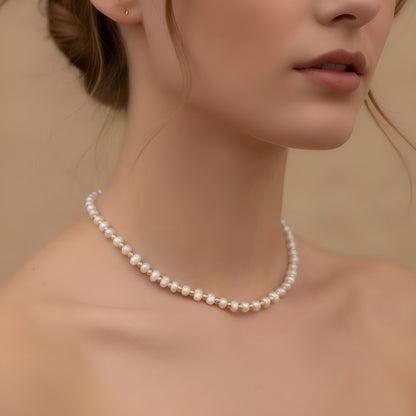 A model wearing the gold bead and pearl station necklace layered with a white shirt, showing the dainty choker length on the neck.