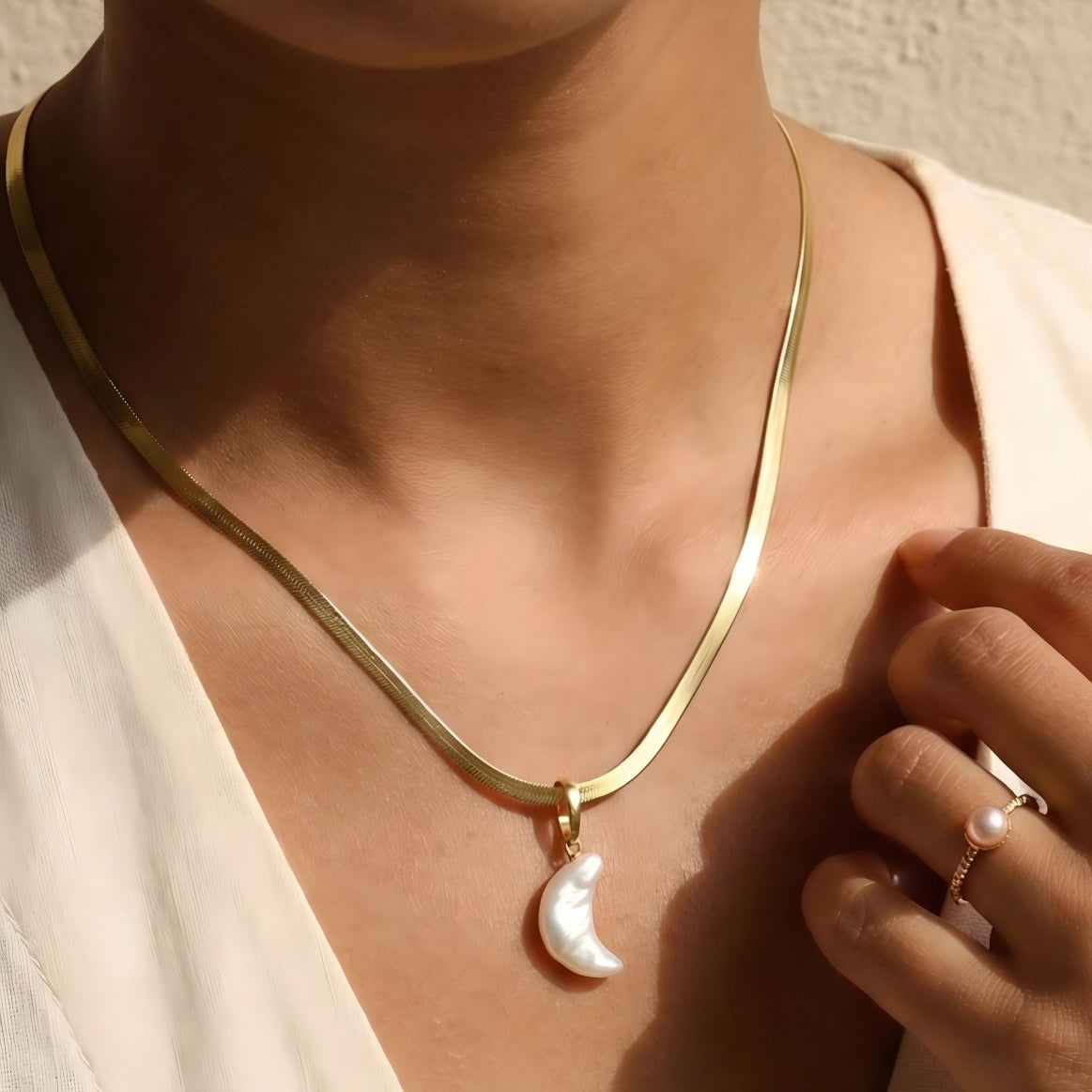 A model wearing the Luna moon pearl necklace with a linen top, bathed in warm sunlight.