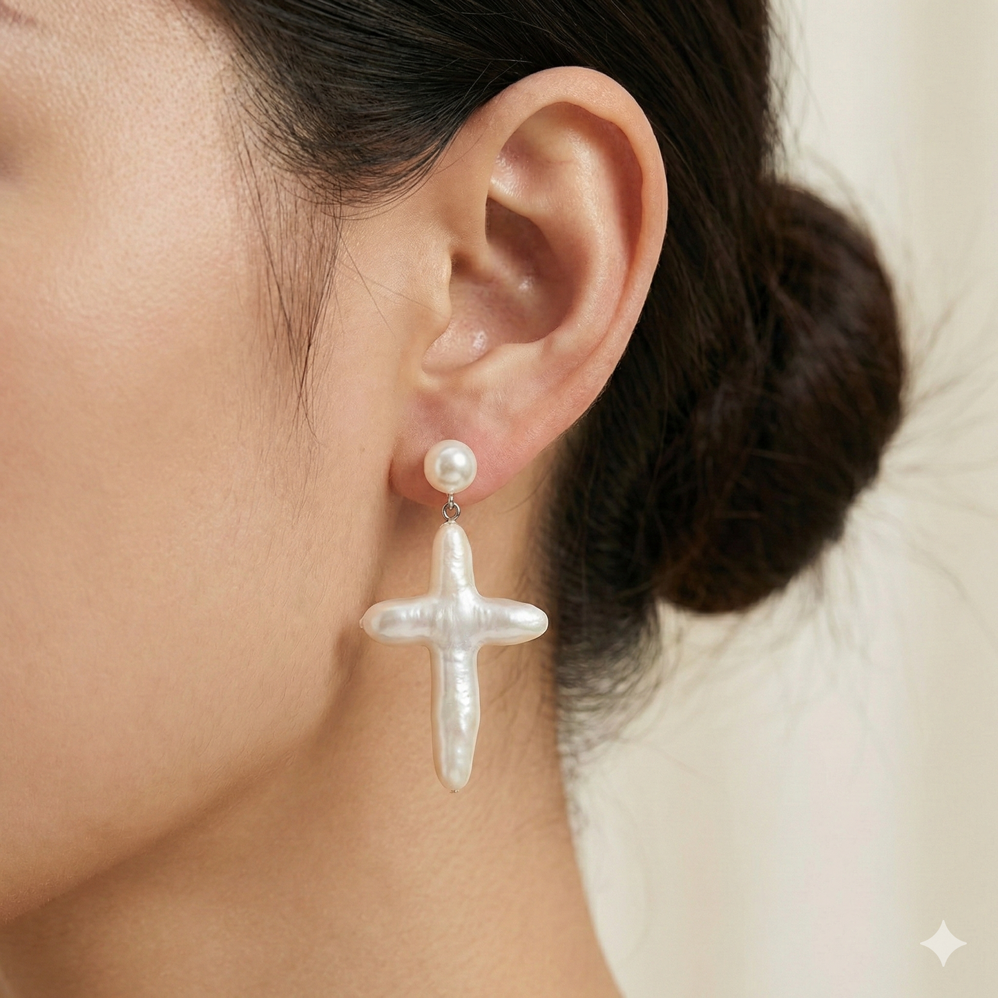 A woman wearing a matching set of organic pearl cross earrings and necklace, styled with a minimalist white blouse.